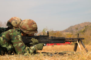 Soldier lying down prone and shooting an M249 SAW light machine gun with the folding bipod down.